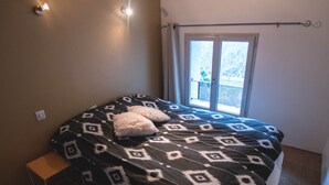 Ein Schlafzimmer mit Bett, einem kleinen Nachttisch, einem Fenster mit Vorhängen und einem Holzbalken an der Decke.