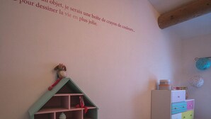 Ein Kinderzimmer mit Holzbalkendecke, einem grünen Bücherregal, einer weißen Kommode und einem farbenfrohen Streifen Teppich.