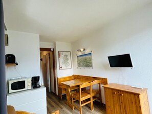 A compact room with a wooden table and chairs, a white cabinet, a microwave, and a flat-screen TV mounted on the wall.
