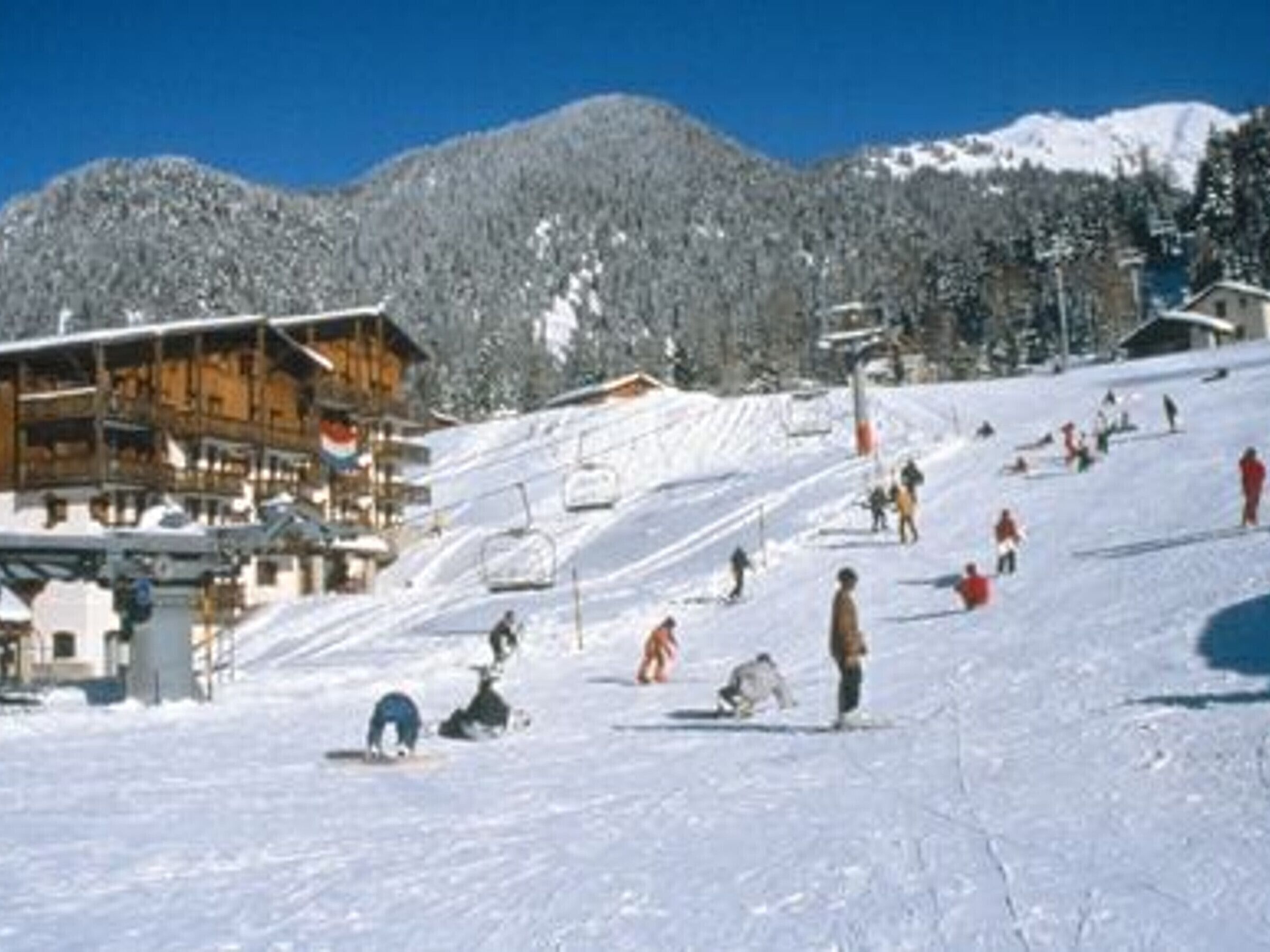 Une station de ski dotée d’un chalet en bois, de remontées mécaniques et d’une piste enneigée où l’on peut voir des skieurs.