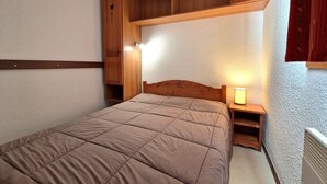 A bedroom with a bed, wooden headboard, built-in shelves, bedside lamps, and a radiator.