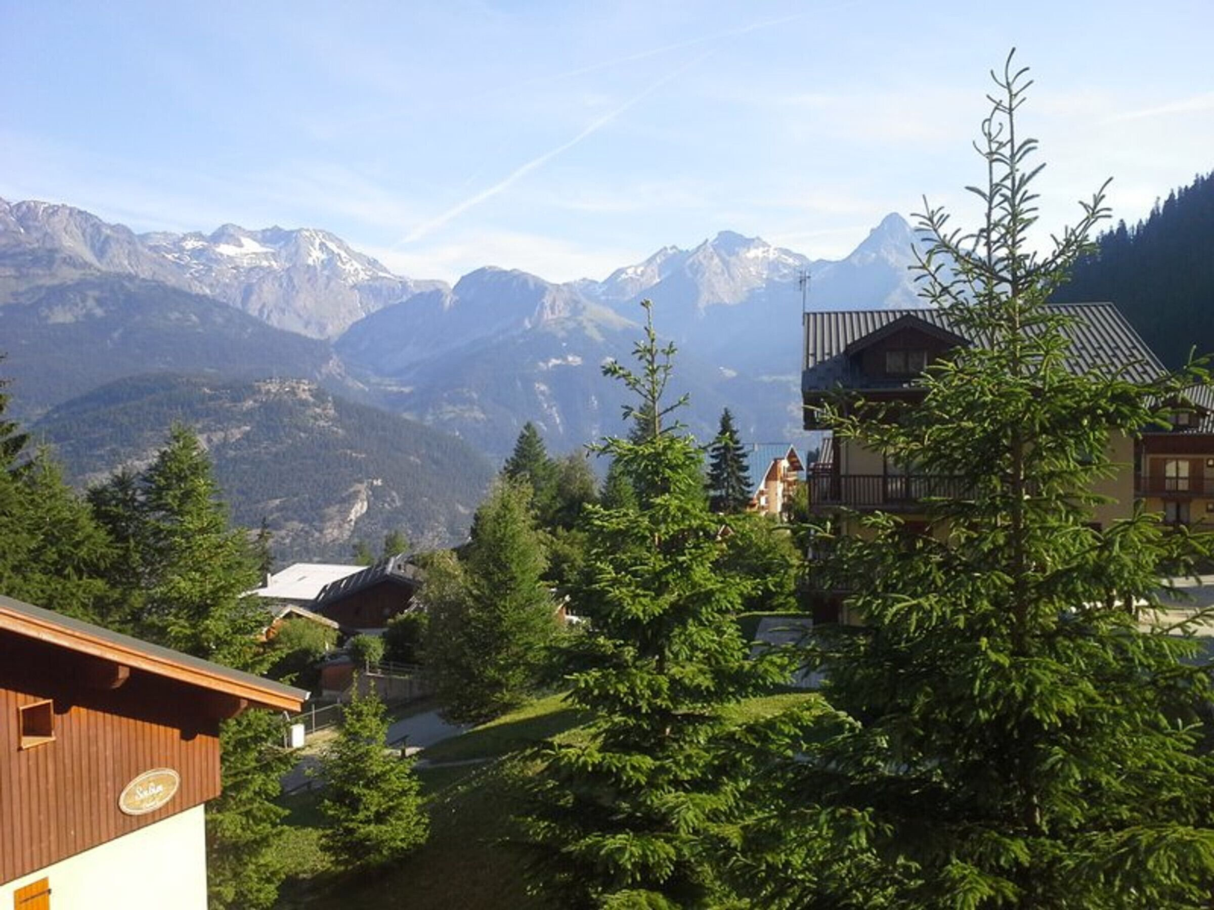 A mountain lodge with a wooden exterior, surrounded by lush greenery and a view of snow-capped peaks.