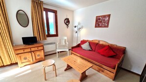 A cozy room with a wooden sofa, a small wooden table, a white chair, a wooden dresser, and a television on a wooden cabinet.