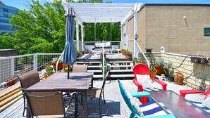 A rooftop patio with wooden tables and chairs, potted plants, and a pergola. - Luxury Loft and Rooftop NOMA Square, Sleeps 8-10 (Greenville)