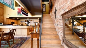A staircase with wooden steps leading to a second floor, a kitchen area with wooden cabinets and a dining table, and a colorful rug on the floor. - Luxury Loft and Rooftop NOMA Square, Sleeps 8-10 (Greenville)