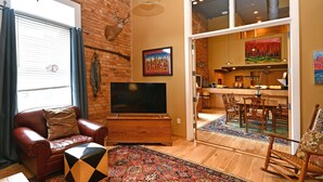 A living room with a leather sofa, a flat-screen TV, a patterned rug, and a deer head mounted on the wall. - Luxury Loft and Rooftop NOMA Square, Sleeps 8-10 (Greenville)