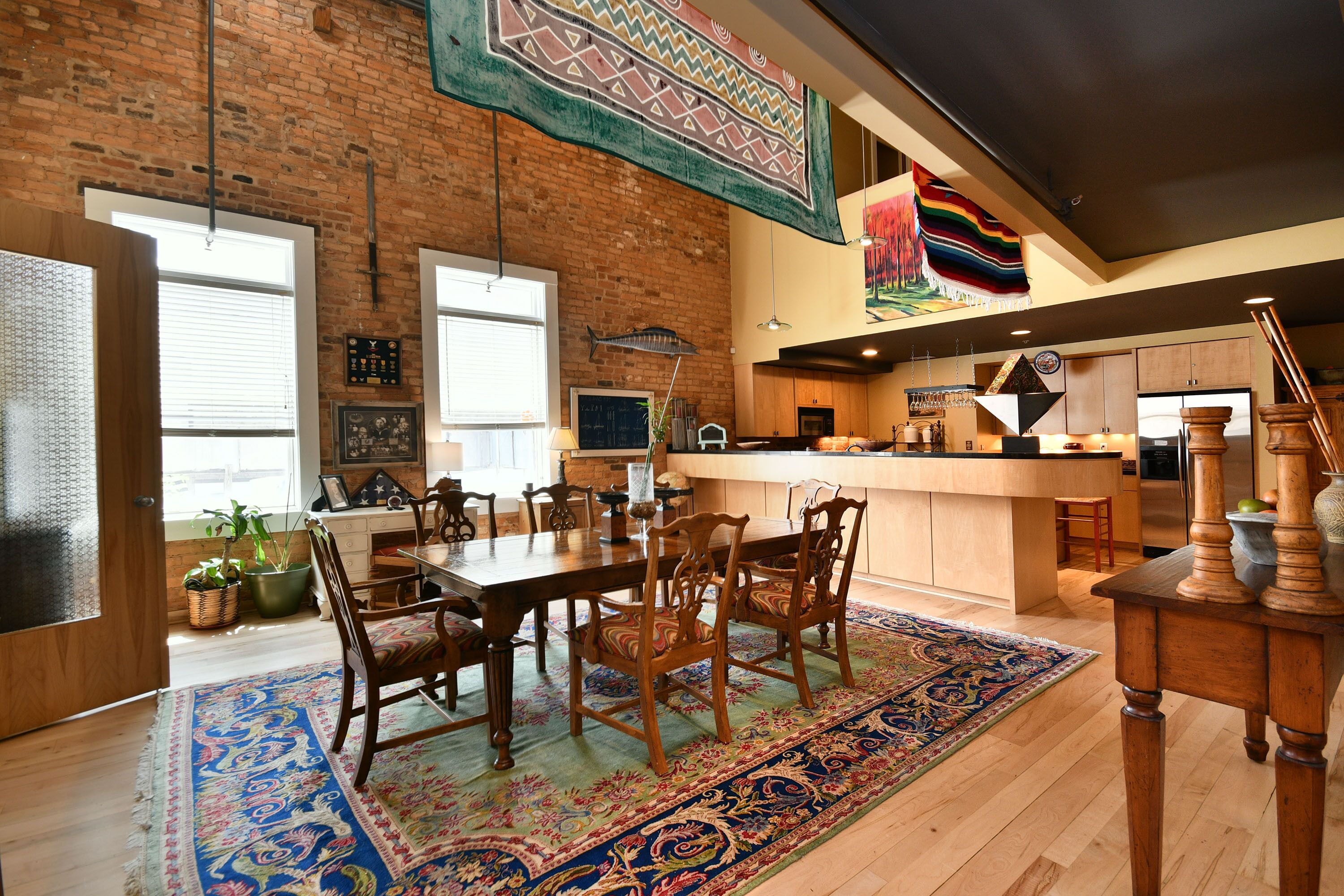 A spacious dining area with a wooden table and chairs, a patterned rug, and a kitchen in the background.