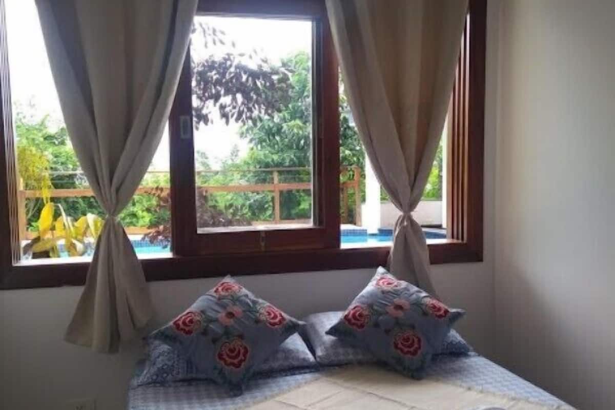 A bedroom with a bed, curtains, and a window with a view of greenery.