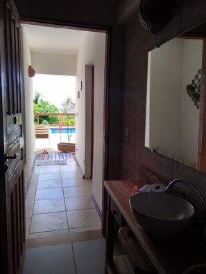 A bathroom with a wooden vanity, a sink, and a mirror. There is a door leading to a balcony with a view of greenery.