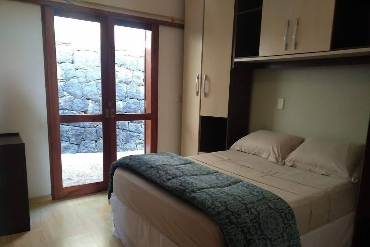 A bedroom with a bed, a wardrobe, and a sliding glass door leading to a stone wall outside.