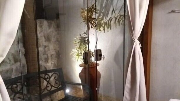 Una habitación con puerta de vidrio, una planta en maceta, un banco de madera y una pequeña mesa con un libro.