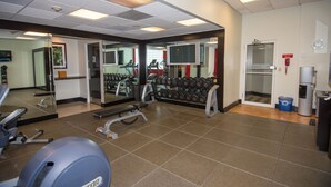 Ein Fitnessstudio mit Trainingsgeräten, einem Spiegel und einem Fernseher.