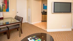 Ein Hotelzimmer mit Esstisch, einem an der Wand befestigten Fernseher und einer durchgehenden Tür erkennbaren Küchenzeile.