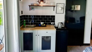 A modern kitchen with a sink, countertop, and a kettle. There is a black refrigerator, a black cabinet, and a shelf with kitchen items. - My Shadows – Elegant Stay Close to Eagle Beach (Oranjestad)