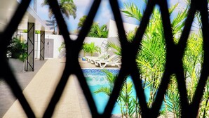 A pool area with lounge chairs and palm trees, viewed through a geometric window frame. - My Shadows – Elegant Stay Close to Eagle Beach (Oranjestad)
