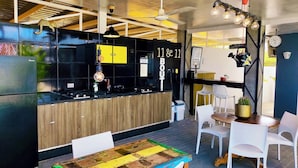 A modern kitchen with a wooden countertop, a black backsplash, and a black refrigerator. There are white chairs and a table with a colorful table runner. - My Shadows – Elegant Stay Close to Eagle Beach (Oranjestad)
