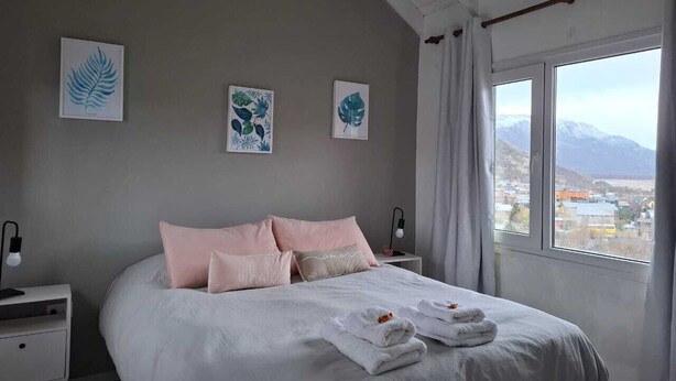 Quarto com uma cama grande, duas mesas de cabeceira e janela com vista para a montanha.