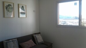 Um quarto com janela, um sofá e duas gravuras botânicas emolduradas na parede.