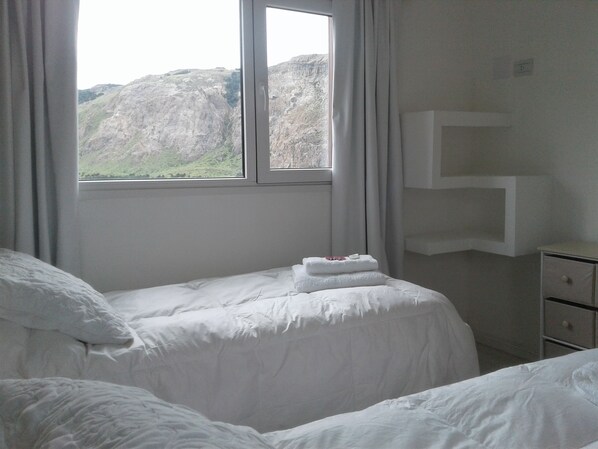 Un dormitorio con cama, cortinas en una ventana y una mesita de noche blanca.