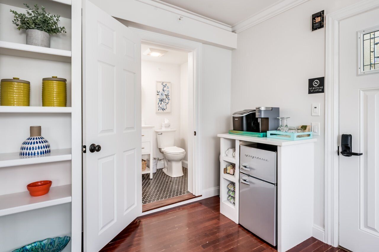 Una cocina compacta con armarios blancos, cafetera integrada y refrigerador.