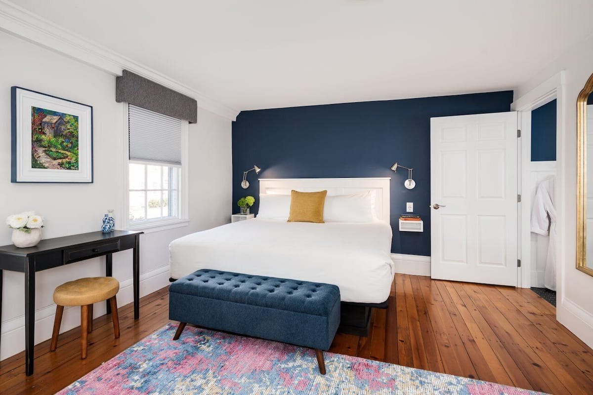 A bedroom with a large bed, a desk, a chair, and a colorful rug.
