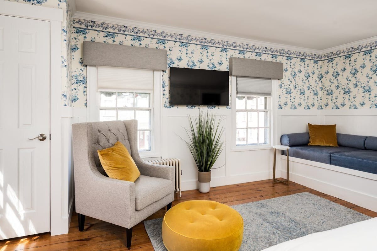 A room with a grey armchair, a blue sofa, a yellow ottoman, and a large potted plant.