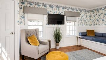 A room with a grey armchair, a blue sofa, a yellow ottoman, and a large potted plant.