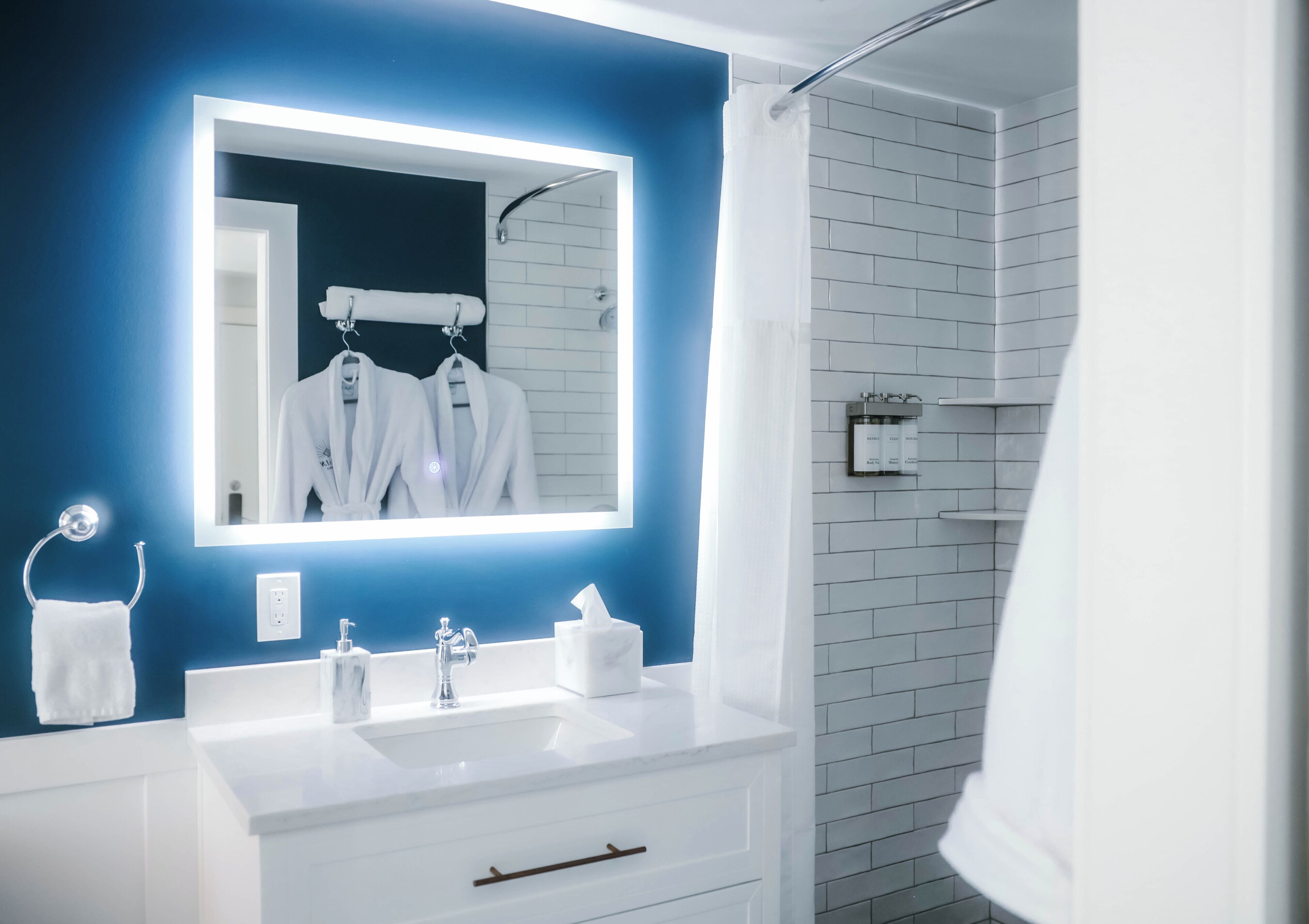 Un baño moderno con una pared azul de acento, un espejo grande, accesorios blancos y una zona de ducha.