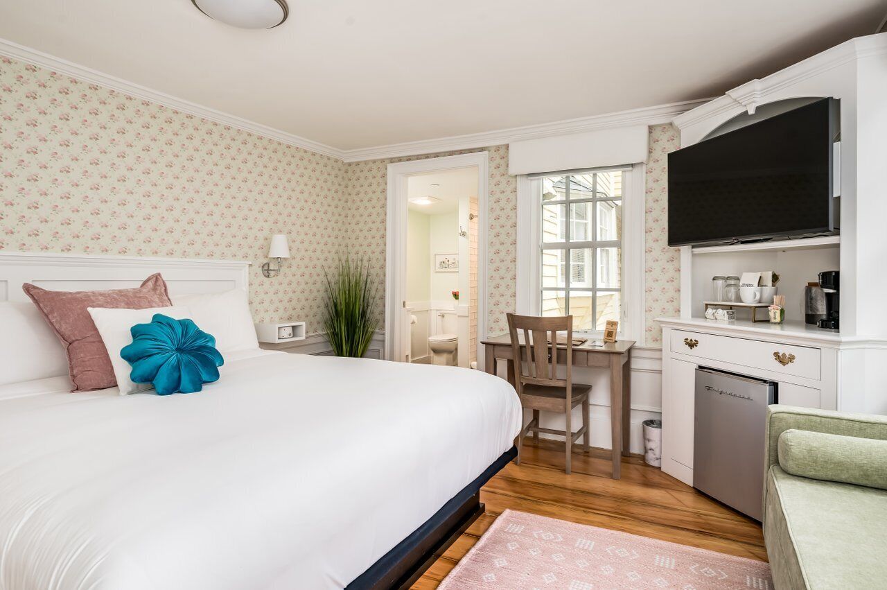 A hotel room with a large bed, a desk, a television, and a kitchenette.