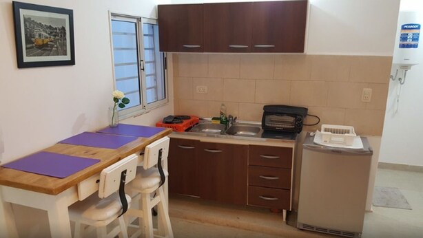 Una cocina compacta con una mesa de madera, dos sillas, un lavabo, un tostador y un refrigerador.