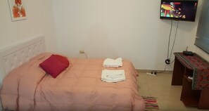 Een slaapkamer met een bed, een televisie aan de muur en een klein houten tafeltje met een tafelkleed met patroon.