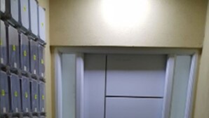 Un pasillo estrecho con una puerta al final, flanqueado por una hilera de armarios con etiquetas amarillas.