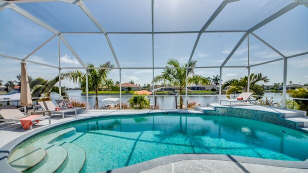 A swimming pool with a clear blue water, surrounded by lounge chairs and palm trees.