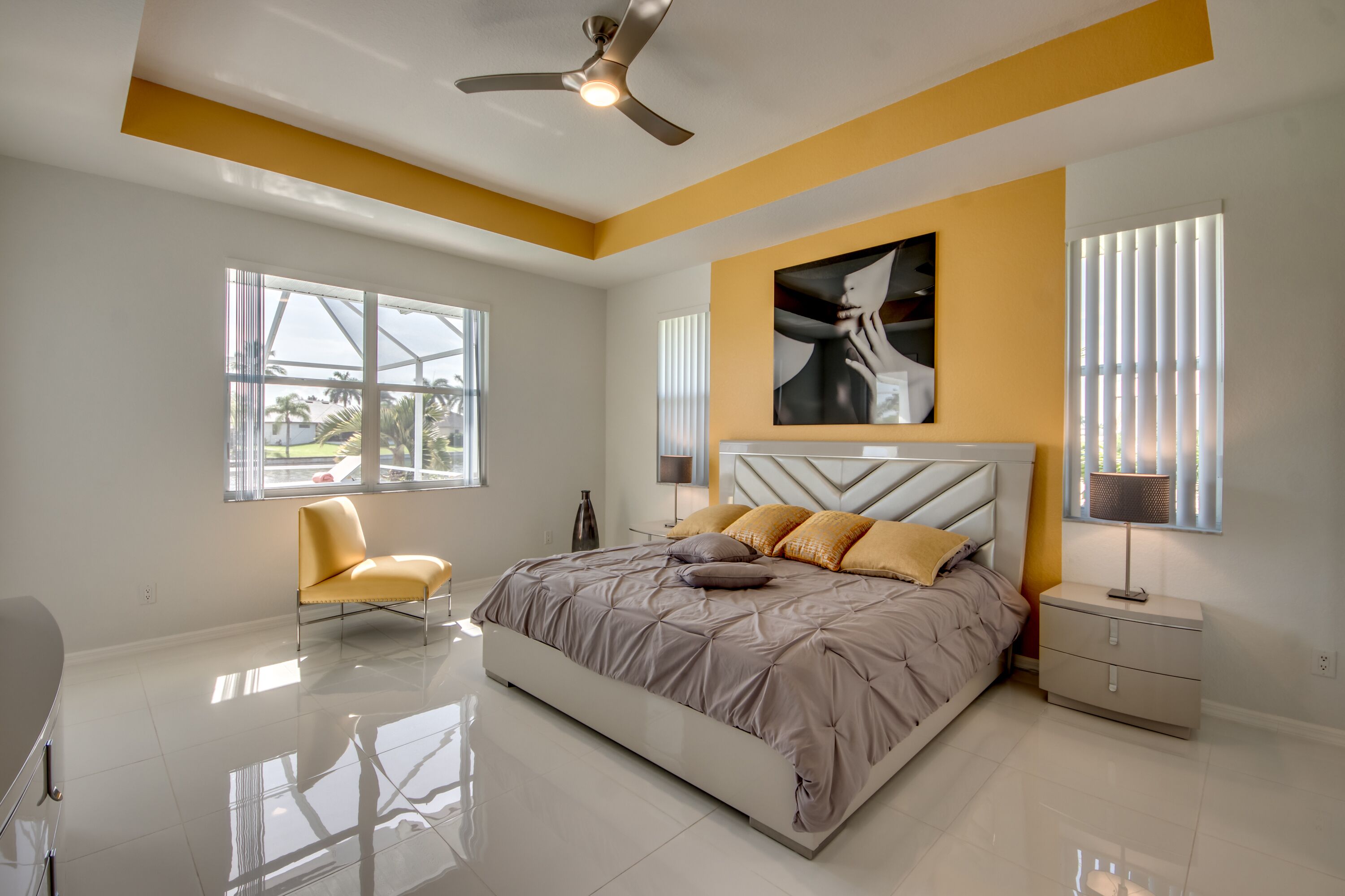 A modern bedroom with a large bed, a chair, a nightstand, and a ceiling fan.