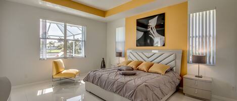 A modern bedroom with a large bed, a chair, a nightstand, and a ceiling fan.