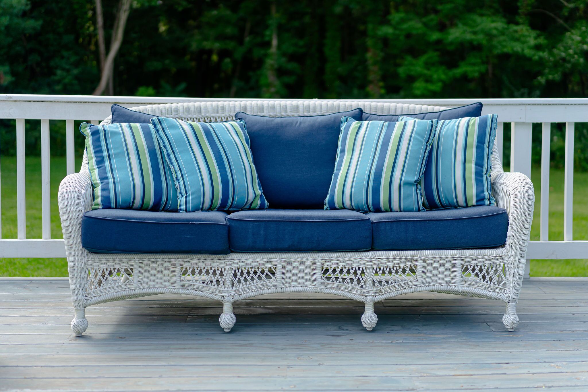 A white wicker sofa with blue cushions on a wooden deck.