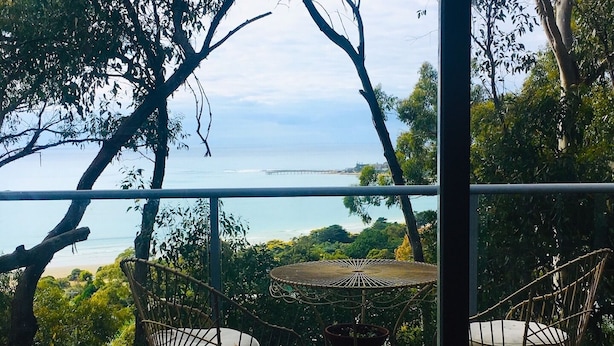 Un balcon avec des fauteuils en osier et une petite table, donnant sur une plage et l’océan.