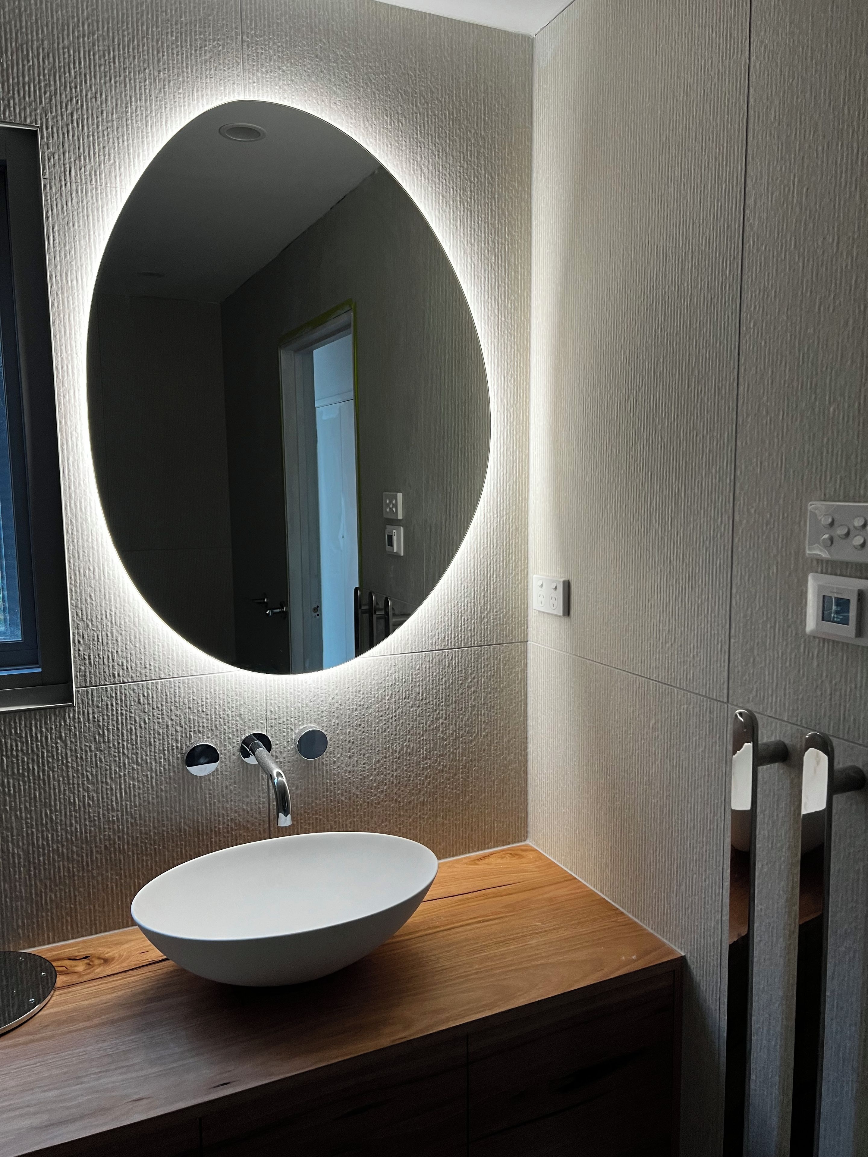 A modern bathroom with a round mirror, a white sink, and a wooden vanity.