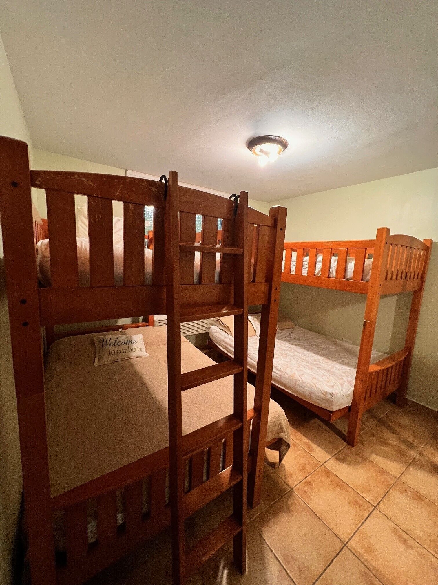 A room with three bunk beds, a ceiling light, and a welcome sign on the lower bunk.