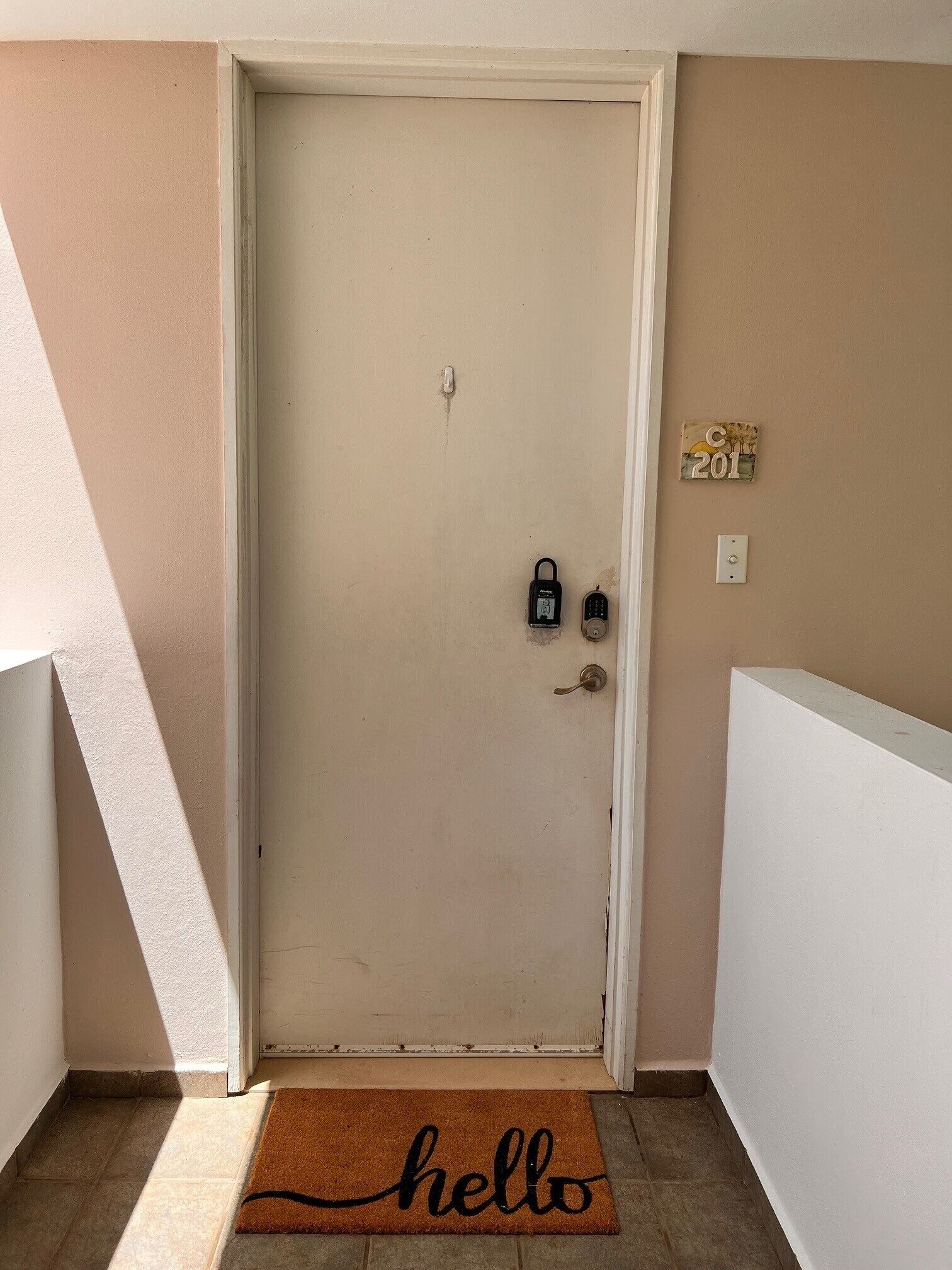 A door with a doormat reading "hello," a mailbox, and a wall-mounted number plate.