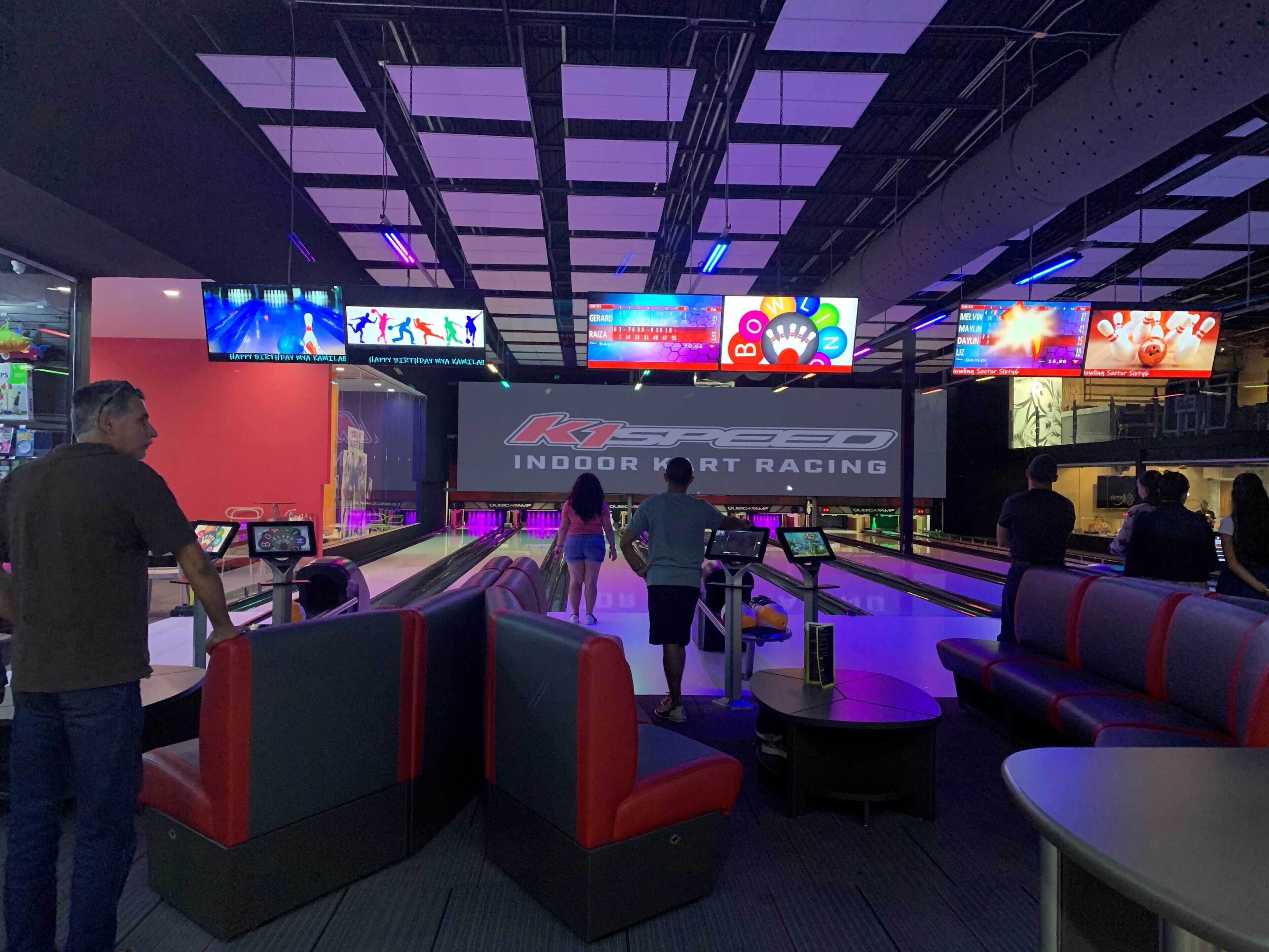 Un bowling intérieur doté de nombreuses pistes, d’espaces pour s’asseoir et d’écrans numériques affichant les scores, placés au-dessus des pistes.