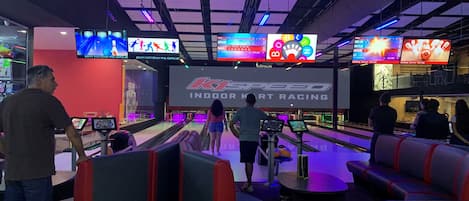 An indoor bowling alley with multiple lanes, seating areas, and overhead digital scoreboards.