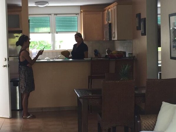 A kitchen with wooden cabinets, a window with blinds, a dining area with a table and chairs, and a refrigerator.