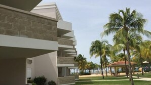 Un hotel moderno con techo plano, balcón y vista a palmeras y playa.