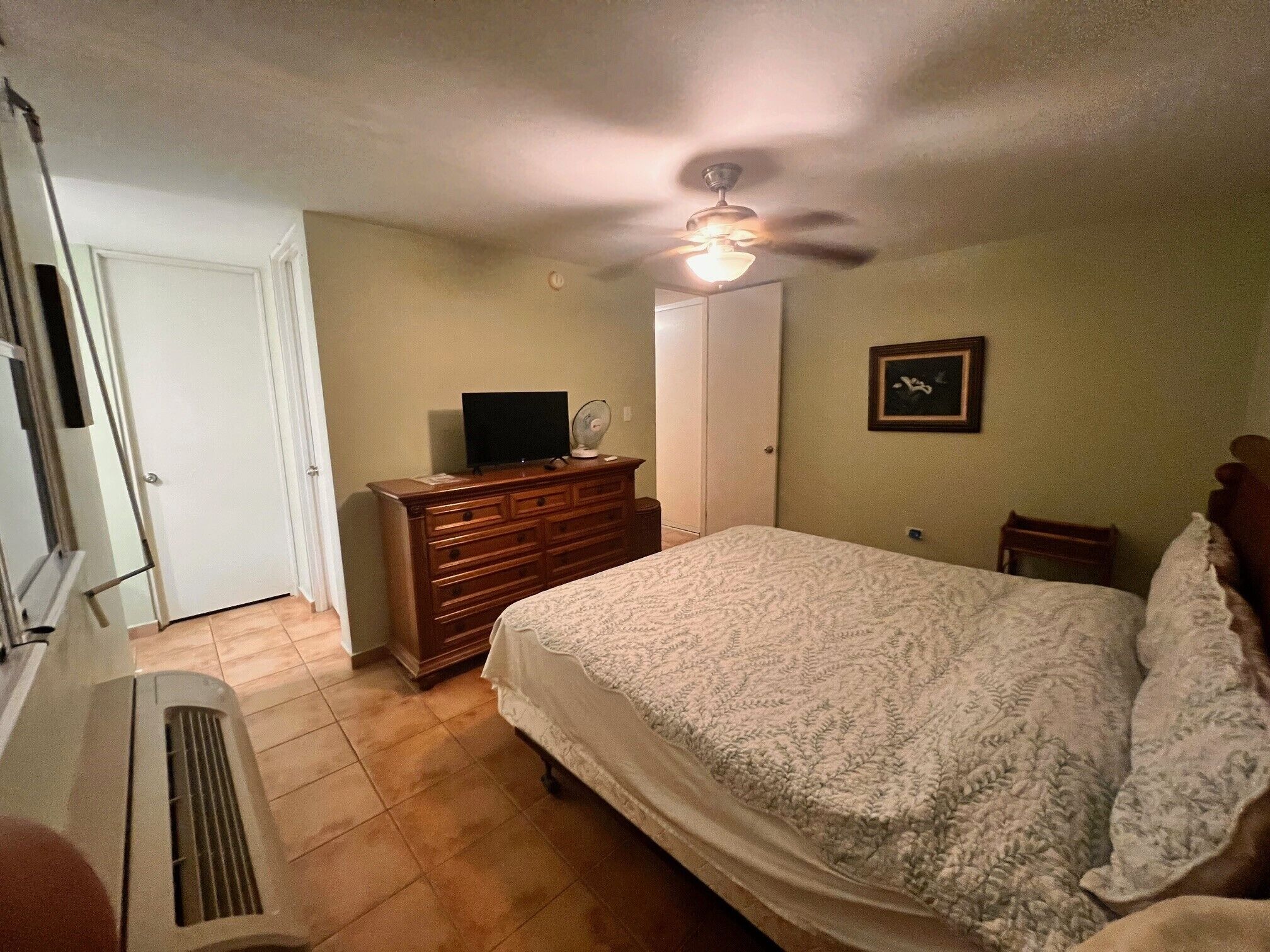 Ein Schlafzimmer mit Bett, Schminktisch, Fernseher und Deckenventilator.