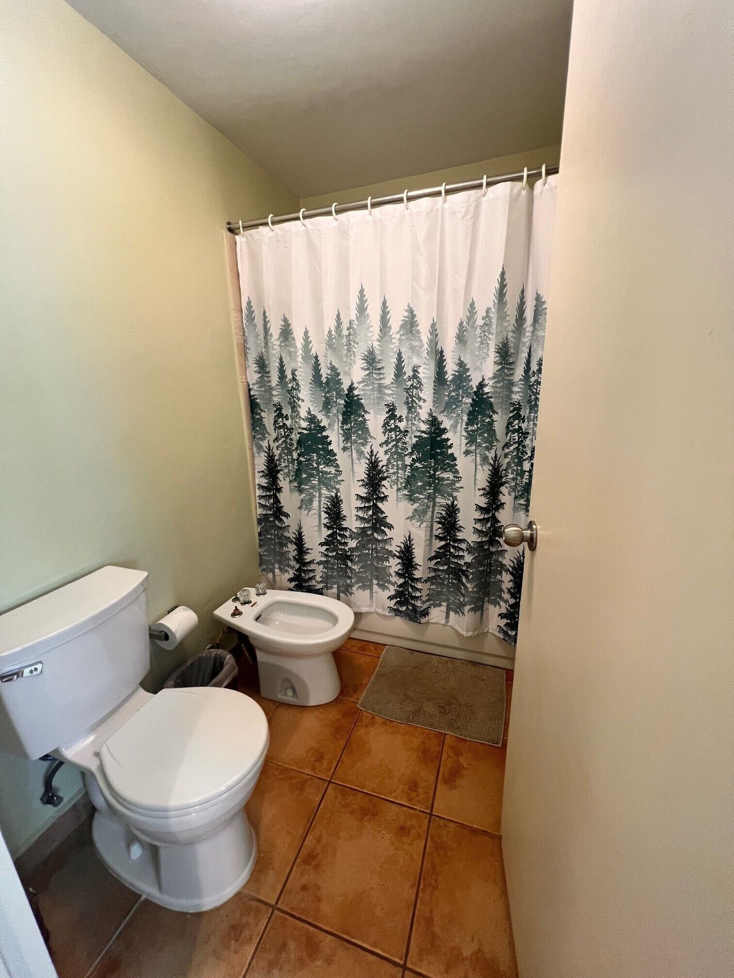 Un baño con inodoro, bidé y cortina de ducha con diseño de bosque.