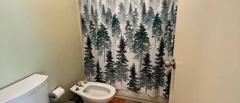 Un baño con inodoro, bidé y cortina de ducha con diseño de bosque.