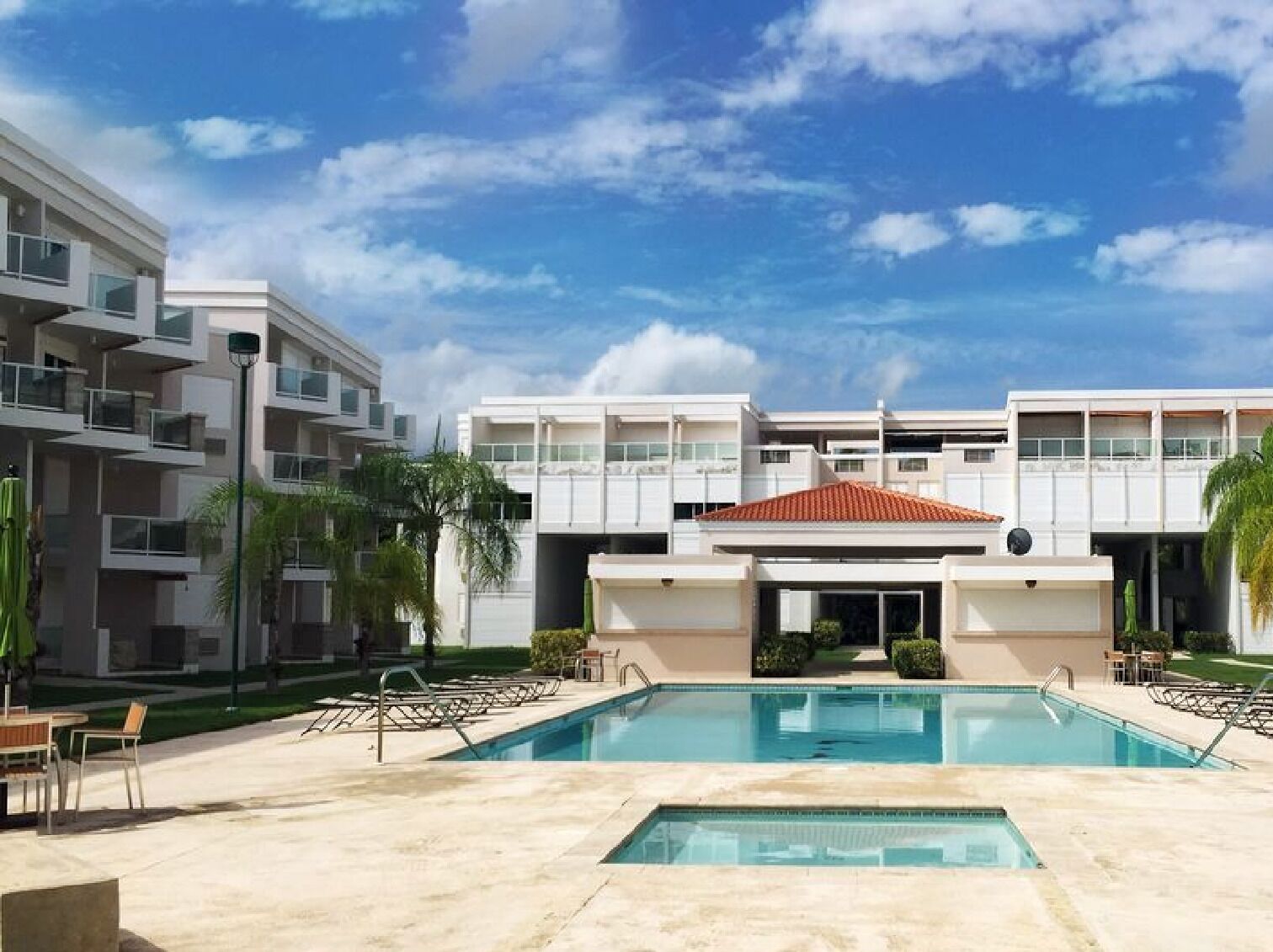 A modern building with a swimming pool, surrounded by palm trees and a clear sky.