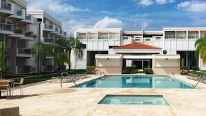 Un hotel moderno con piscina central, varios balcones y un cielo azul despejado.