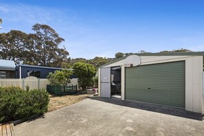 A residential garage with a green shutter, a white picket fence, and a tree in the background.